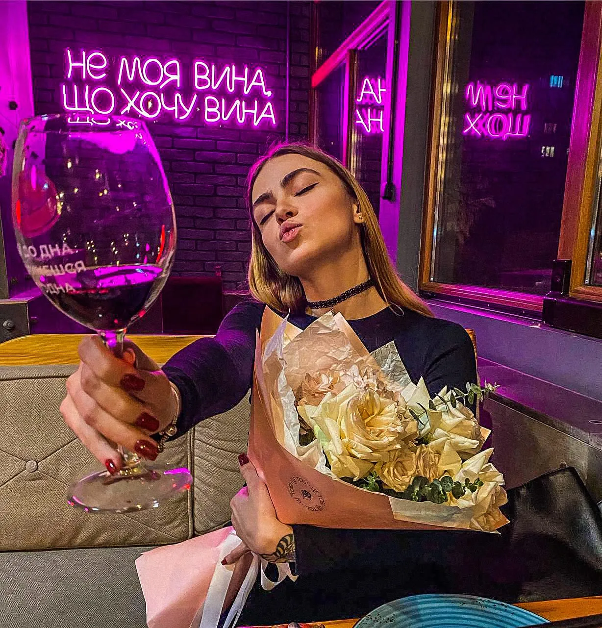 Гостя з великим бокалом вина під неоновим написом «Не моя вина, що хочу вина»